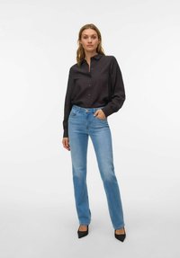 Must värviline pikkade varrukatega nööpidega särk koos peene mustriga, mille kõrvale on pandud helerohelised sirged teksapüksid ja mustad terava ninaga kontsad.