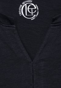 Dunkelblaues Kleidungsstück mit V-Ausschnitt-Design, das kontrastierende Nähte und ein rundes Logo mit dem Text "CREATIVE GETAWAY" in Weiß aufweist.