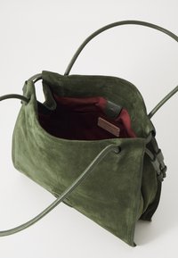 Borsa in suede verde con apertura superiore, foderata in bordeaux. La borsa presenta bordi morbidi e due manici lunghi e sottili per il trasporto.