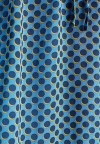 Tissu bleu avec un motif répétitif de cercles bleu foncé partiellement entourés de jaune, avec un cordon visible sur le côté droit.