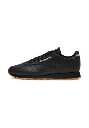 Black Reebok leather sneaker with gum sole, lace-up design, and Reebok logo with British flag on the side.