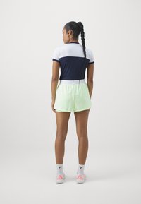 Marint och vitt färgblockerat åtsittande linne i kombination med ljusgröna shorts med elastisk midja. Modell bär vita och rosa träningsskor.