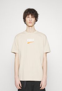 Beige katoenen T-shirt met korte mouwen en een ronde hals. Voorzien van een geborduurd oranje en wit "PUMA" logo op de borst.