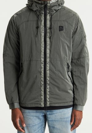 Leichte Kapuzenjacke in Olivgrün, mit durchgehendem Reißverschluss, elastischen Bündchen und zwei Seitentaschen. Der Stoff hat einen dezenten Glanz und eine Struktur.