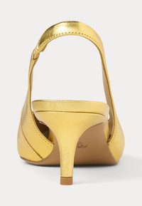 Κίτρινο ψηλοτάκουνο παπούτσι με μεταλλική επίστρωση, ανοιχτή πλάτη, λεπτό τακούνι και καμπυλωτό σχέδιο λουριού. Λείο υλικό με ελάχιστες λεπτομέρειες.