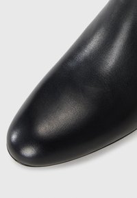 Sapato preto de couro com biqueira pontiaguda e textura suave, apresentando um leve brilho e um contorno aerodinâmico. Sem ferragens ou enfeites visíveis.