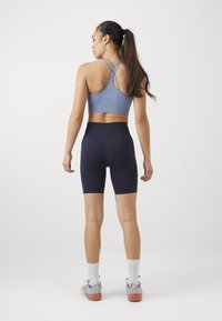 Lys blå sports-bh med kryssende stropper, sammen med mørk marineblå sykkelshorts med lomme og teksturert midjebånd.