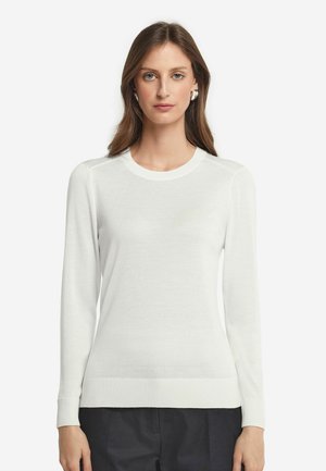 Pull blanc à manches longues avec un col rond, des poignets et un ourlet côtelés. Texture lisse et silhouette ajustée, associé à un pantalon sombre.