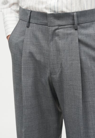 Γκρι παντελόνι με πτυχές, θηλιές για ζώνη και πλαϊνές τσέπες, φορεμένο με λευκό πουκάμισο μακρυμάνικο με λεπτές κάθετες ρίγες.