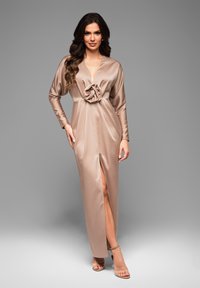 Robe satin longue couleur tan avec un décolleté en V profond, des manches longues et un détail décoratif en forme de rose à la taille ; présente une fente haute à l'avant.