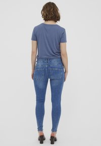 Camiseta azul de manga corta y jeans de mezclilla azul ajustados, con bolsillos traseros y una textura suave. Sandalias de tacón negras completan el look.