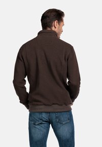 Bruine fleece sweatshirt met een hoge kraag, textuurstof en ribbelboorden. Draagt met blauwe denim jeans, wat een casual pasvorm laat zien.