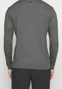 Pitkähihaisen, slim-fit paidan tummanharmaa väri, valmistettu sileästä kankaasta. Paitassa on pieni logo yläselässä ja pyöristetyt sivut.