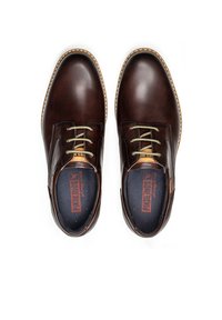 Zapatos de cuero marrón con un acabado liso, costuras en tono contrasta en beige y cordones verdes. Cuentan con una plantilla con marca y un diseño de puntera redonda.