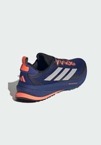 Sininen urheilujalkine, jossa on hengittävä verkkopinta, oranssit yksityiskohdat, hopeiset raidat, pehmustettu pohja ja vetoketju kantapäässä.