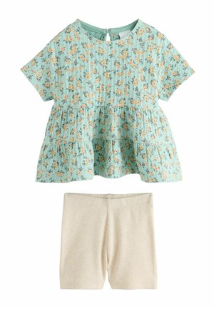 Hellblaues kurzärmeliges florales Oberteil mit gestuften Rüschen, kombiniert mit beigen, gerippten Strickshorts.