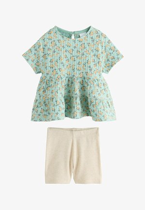 Haut à manches courtes bleu clair à fleurs avec volants superposés, associé à un short en maille côtelée beige.