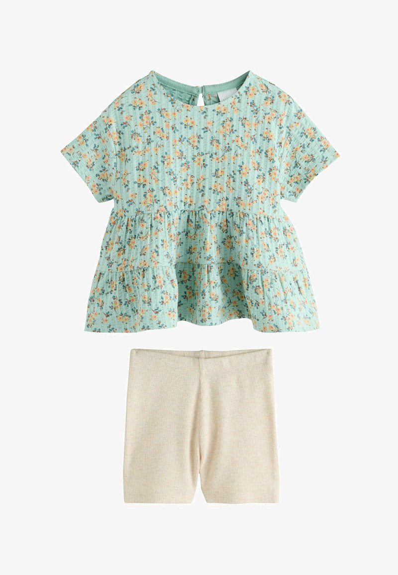 Haut à manches courtes bleu clair à fleurs avec volants superposés, associé à un short en maille côtelée beige.