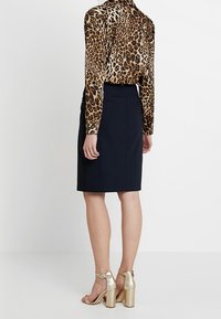 La blouse à imprimé léopard présente des manches longues, associée à une jupe crayon marine longueur genoux et des sandales à talons blocs dorés.