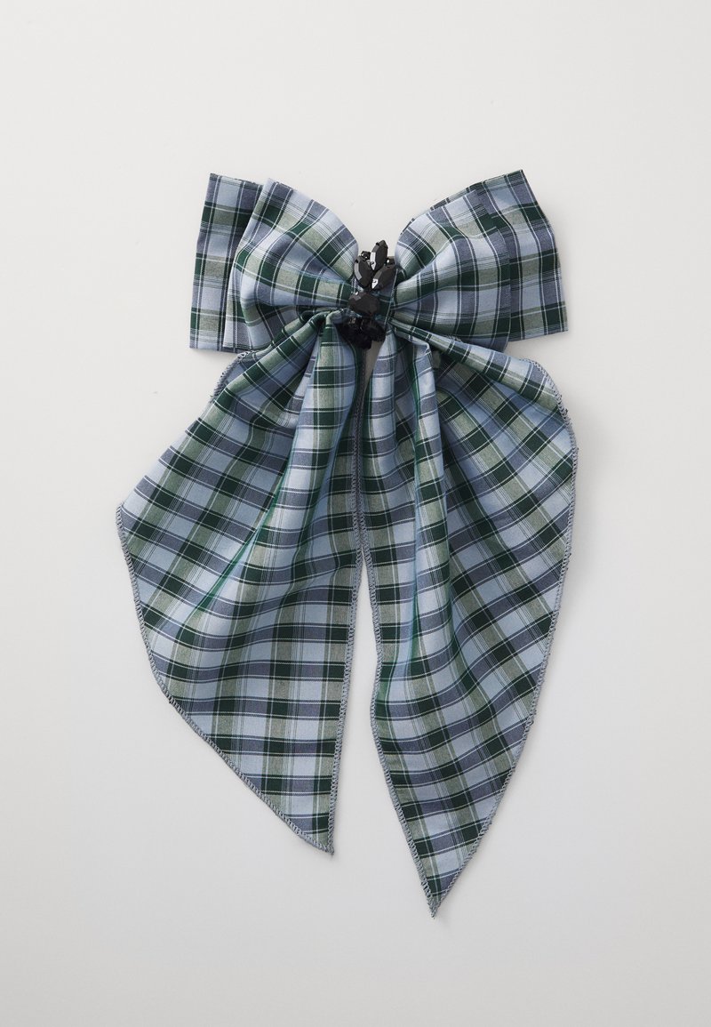 Pika iz karirane tkanine v zeleno-modrih tonih, z obrobno črno sredino in dvema dolgima, ostrima repoma.