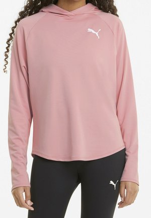 Femme portant un haut à capuche rose à manches longues et un legging noir, tous deux avec un logo Puma blanc sur la poitrine et la cuisse.