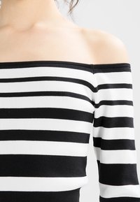 Schulterfreies Oberteil mit horizontalen Schwarz-Weiß-Streifen, gerippter Textur und figurbetontem Design mit weitem Ausschnitt.