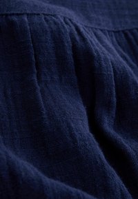 Tissu froissé bleu foncé avec une apparence texturée et tissée, et des coutures froncées créant des plis et des ombres.