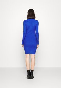 Stickad klänning med långa ärmar i klarblått, med en figurnära form och ribbad textur, parat med svarta klackade ankelskor.