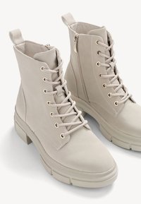 Bottes beiges à lacets avec fermetures éclair latérales, languettes de tirage et semelles en caoutchouc épaisses, vues en plongée sous un angle.