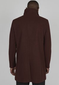 Barna gyapjú kabát magas gallérral és karcsú dizájnnal. Egyenes szabású, minimalista varrással a háton.