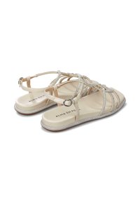 Sandalias beige con acentos de strass, con un diseño de tiras y una suela plana y brillante. Hebilla ajustable en el tobillo para un mejor ajuste.