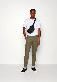 Olívově zelené cargo kalhoty, zúžené u kotníků, ve spojení s jednoduchým bílým tričkem a černou crossbody taškou. Černé nízké tenisky.