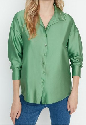 Blusa di raso verde con collo a camicia, maniche lunghe e chiusura a bottoni. La texture liscia e la leggera lucentezza ne esaltano l'appeal visivo.