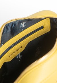 Interno di una borsa in pelle gialla con una tasca con zip nera. Il tessuto interno presenta un delicato motivo a logo blu con una superficie liscia.