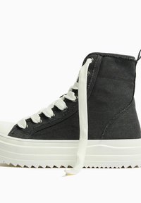 Wysokie trampki wykonane z czarnego płótna z białym gumowym noskiem i podeszwą, z białymi sznurowadłami i zygzakowatym wzorem bieżnika.