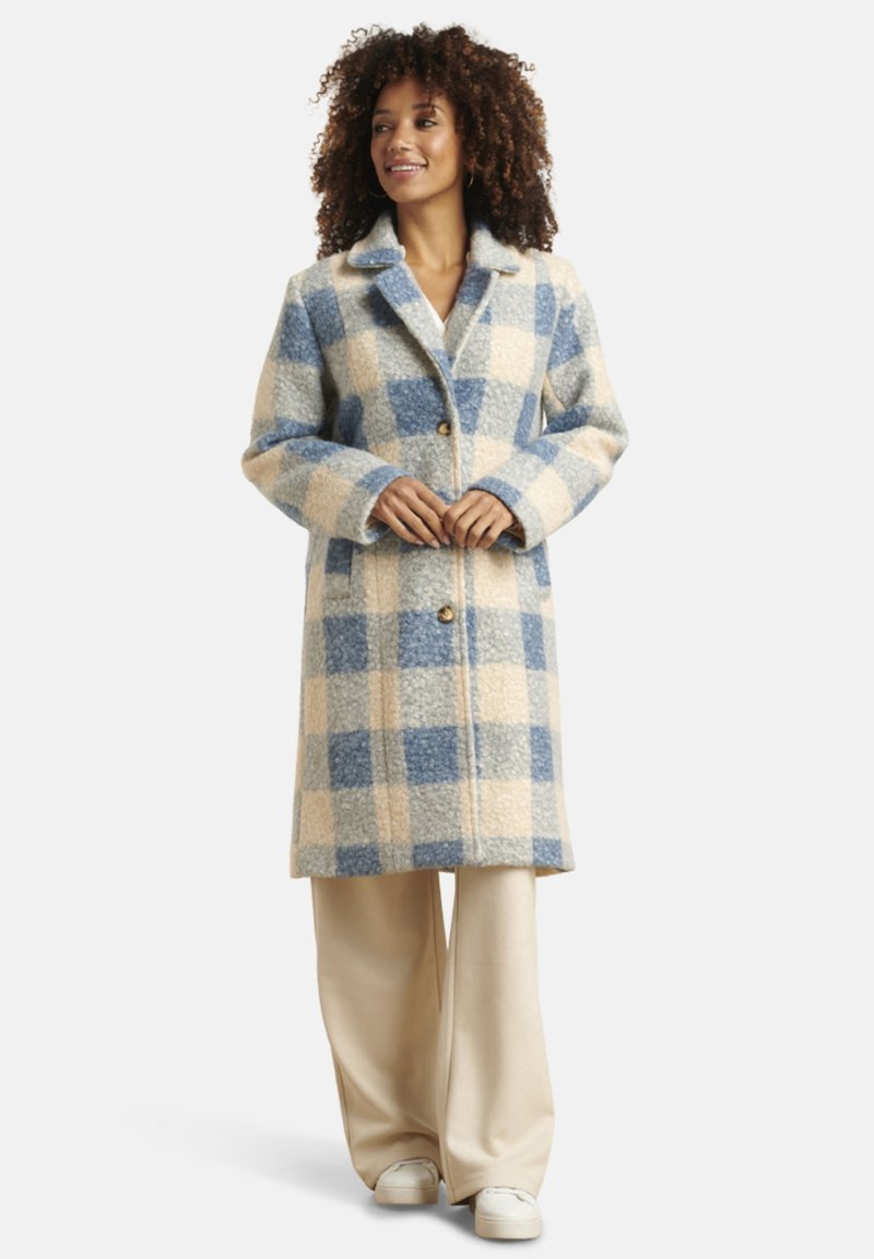 Karierter Wollmantel in Blau- und Cremetönen, mit Reverskragen, Frontknöpfen und knie-langer Passform. Getragen über cremefarbenen weiten Hosen.