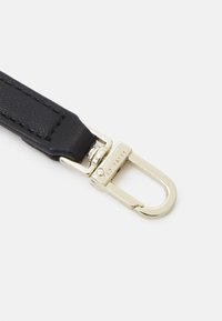 Bracelet en cuir noir texturé avec une boucle métallique dorée, présentant une forme rectangulaire et un détail de marque gravé sur le fermoir.