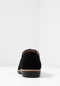 Chaussure noire en daim à lacets, profil bas avec un bout rond, semelle beige et de subtils détails de couture sur le talon et la tige.