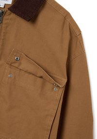 Braune Canvasjacke mit einem Cordkragen, ausgestattet mit einer sichtbaren Druckknopftasche und einem Reißverschluss, der strapazierfähigen Stoff und praktisches Design betont.