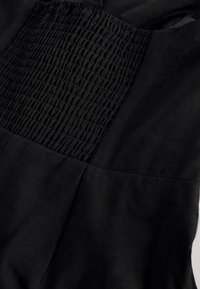 Tissu noir avec un panneau élastique smocké et des sections lisses, montrant une texture froncée et des détails de couture.