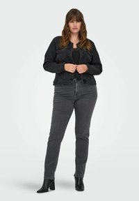 Svart denimjacka med knäppning, två bröstfickor och lång ärm, kombinerad med svarta åtsittande jeans och ankelstövlar.