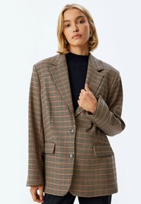 Karierter Blazer in Beige-, Braun- und Rosttönen. Mit Reverskragen, zwei Vorderaschen und zwei Knöpfen sowie einer lockeren Passform.