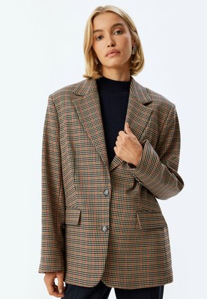 Blazer a scacchi in toni beige, marrone e ruggine. Caratterizzato da un colletto a rilascio, due tasche frontali e due bottoni, con una vestibilità rilassata.