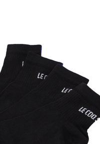 Calcetines negros con textura acanalada y texto blanco "LE CODE" en el puño. Incluye un acento azul en la parte superior del puño.