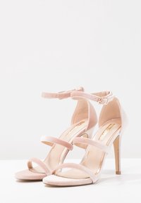 Vaaleanpunaiset samettiset korkokengät, joissa on kaksi vaakasuoraa remmiä varpaiden ylle ja säädettävä nilkkaremmi. Hoikka stilettokorko. Sujuva pinta.