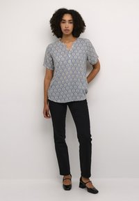 Blouse à manches courtes bleue à motifs avec un décolleté en V, assortie à un pantalon slim noir et des chaussures à talons carrés noires.