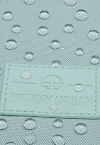 Tessuto di un verde menta chiaro con una superficie texture, caratterizzato da gocce d'acqua e un'etichetta in pelle cucita con la scritta "JOHNNY URBAN" in rilievo.