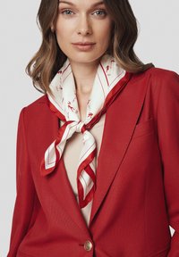Czerwony żakiet z teksturowanej tkaniny, zestawiony z białym jedwabnym szalikiem w czerwone paski i małe wzory. Szalik elegancko zawiązany na szyi.