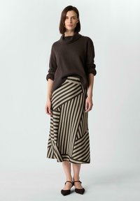 Dunkelbrauner Rollkragenpullover, kombiniert mit einem gemusterten, knielangen Rock, der abwechselnd Streifen in Khaki und Dunkelbraun zeigt. Braune Ballerinas.