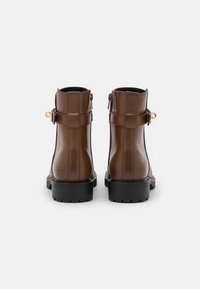 Bottines en cuir marron avec une fermeture éclair sur le côté, semelle plate en caoutchouc noir et une sangle décorative avec une boucle dorée à l'arrière.